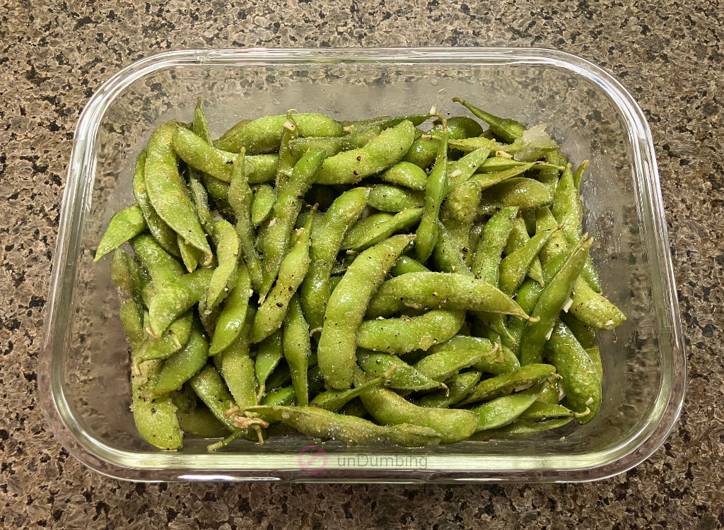 Edamame tossed with olive oil, garlic, sea salt, and black pepper in a rectangular glass container